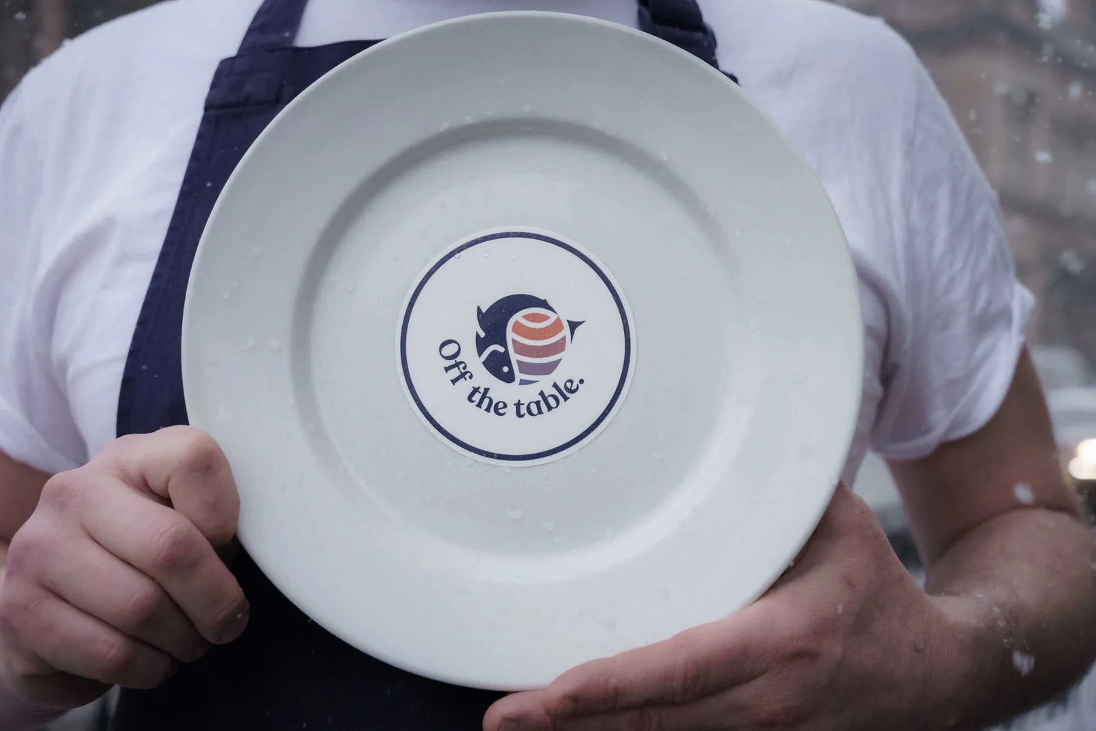 A chef holding an Off The Table campaign card in their kitchen